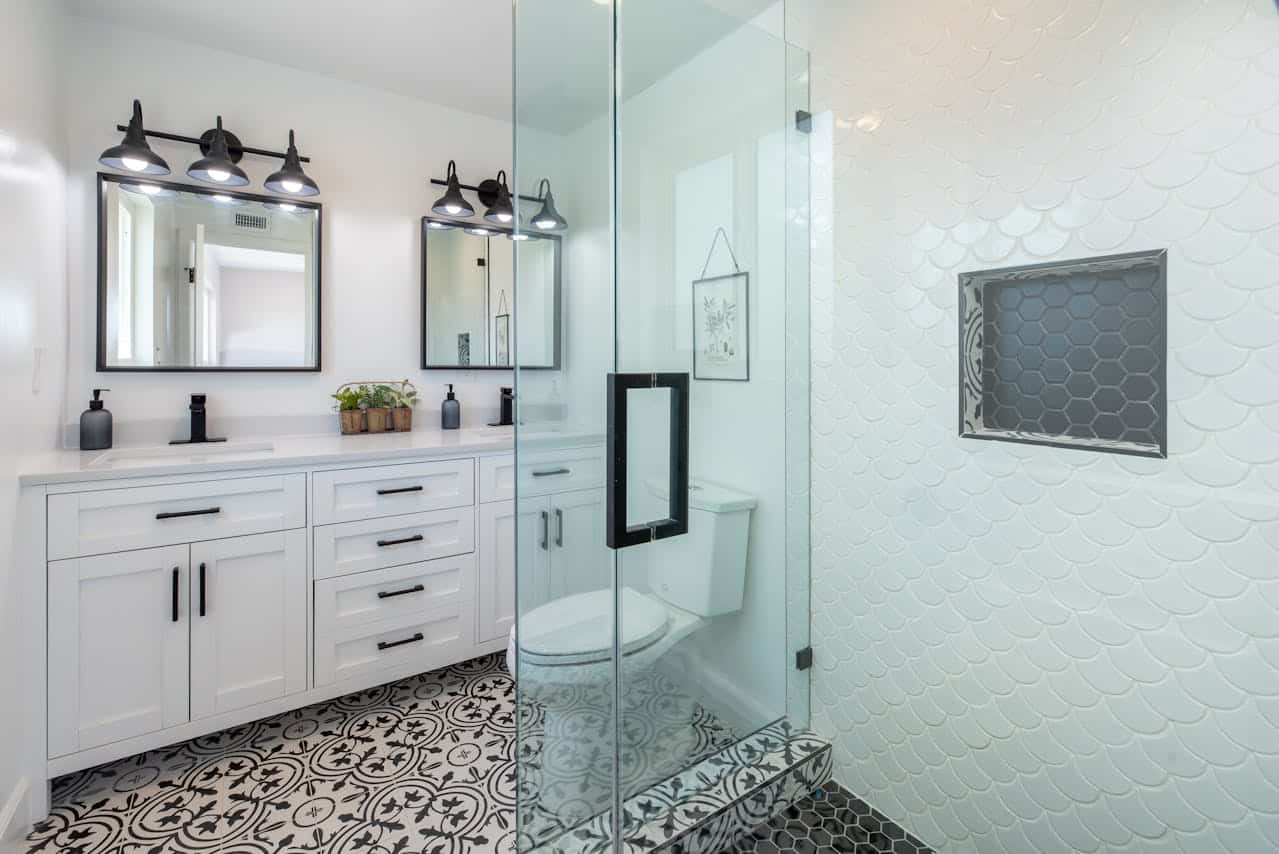 Modern Tile Bathroom Remodel Modern bathroom with patterned tile flooring, glass shower enclosure, white cabinetry, and black fixtures.