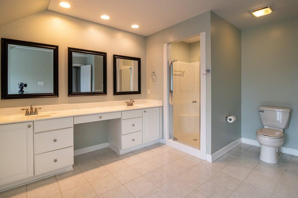 Spacious bathroom with double-sink white vanity, framed mirrors, walk-in shower, and soft overhead lighting.