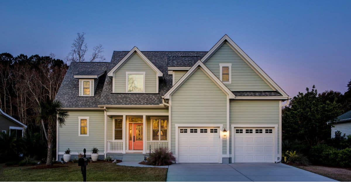 Enhancing Curb Appeal Through Exterior Remodeling A two-story suburban home with sage green siding, white trim, a coral-colored front door, and a two-car garage under a twilight sky.