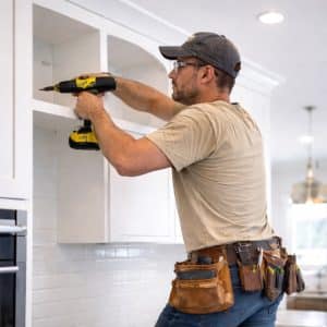 installer securing kitchen cabinet with drill