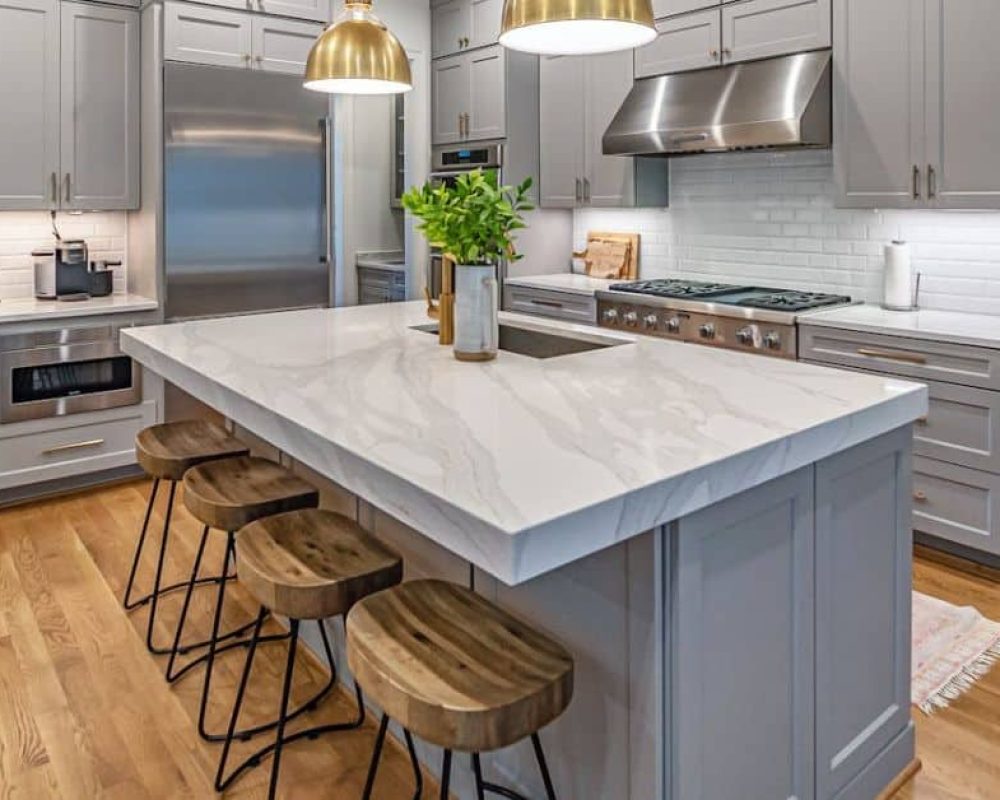 Custom kitchen island with marble countertop and wooden stools surrounded by gray cabinets in a modern Port St. Lucie kitchen.