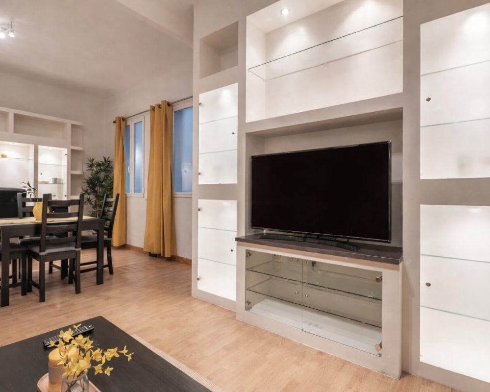 Modern living room with custom built-in TV cabinetry and shelving beside a dining area