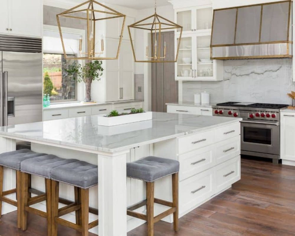 White custom kitchen island with gray cushioned stools, marble countertop, and gold lighting fixtures in a modern Florida kitchen.